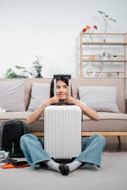 Oturma odasında bavuluyla oturan gülümseyen kadın seyahat için hazırlanıyor. Rahat ve rahat bir ortam..