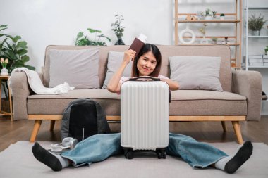 Çantası ve pasaportuyla gülümseyen kadın, rahat bir oturma odasında oturuyor, seyahat macerasına hazır..