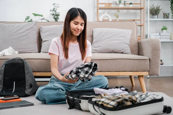 Gülümseyen kadın bir bavul içinde giysilerini düzenliyor, rahat bir oturma odasında geziye hazırlanıyor..