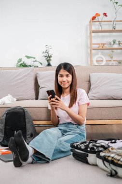 Genç bir kadın yerde oturuyor, parlak, modern bir oturma odasında bavulunu topluyor, seyahat etmeye hazır..