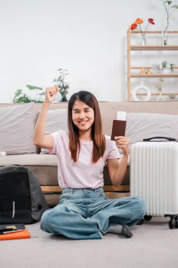 Pasaport ve bavullarıyla yerde oturan gülümseyen kadın, seyahat için heyecanlı. Konforlu oturma odası..