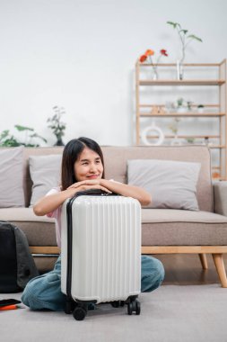 Konforlu oturma odasında bavuluyla gülümseyen bir kadın seyahat için hazırlanıyor..