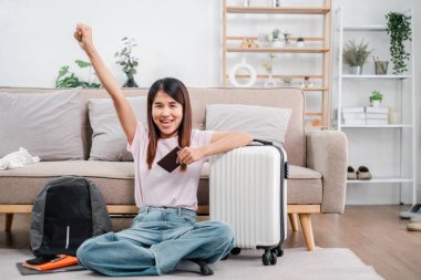 Pasaportu ve bavulu olan neşeli genç bir kadın seyahat macerasına hazır, şık bir oturma odasında oturuyor..