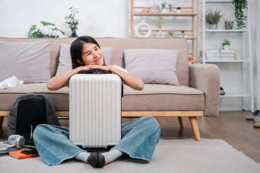 Gülümseyen kadın bavuluyla yerde oturuyor, seyahat macerasına hazır, rahat bir oturma odasında..