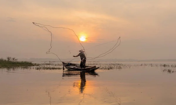 Silhouette of fishermen casting for catching the fish on the wooden boat at the lake in the morning. Thailand lifestyle.