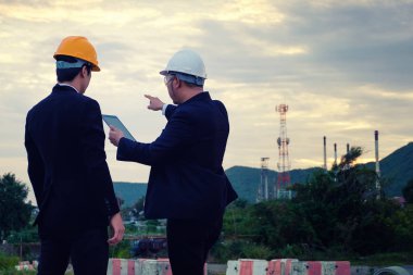 İki mühendis tablet ile saat akşam sanayi arka plan üzerinde çalışıyoruz. Mühendis adamla planlama inşaat müdürü.