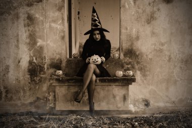 Genç kadın cadı Halloween kılık korkutucu koyu arka plan üzerinde turuncu kabak tutun.