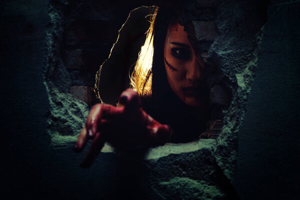 Horror Scene with bloody hand of evil is coming from a dark hole. Halloween concept. Focus at face.