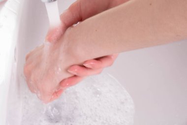 Kız ellerini banyoda musluğun altında sabunla yıkıyor.