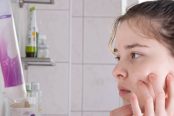 young girl washes her face and looks in the mirror in the bathroom in the morning