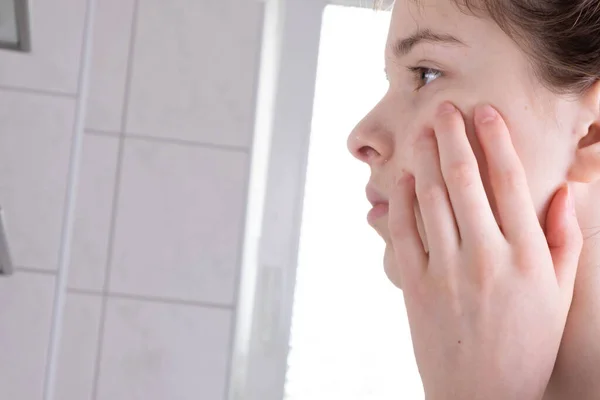 girl washes her face and looks in the mirror in the bathroom in the morning