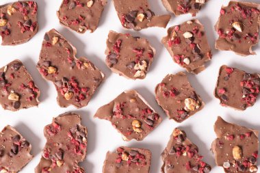 Ahududu fındıklı kırık çikolata parçaları bulmaca şeklinde beyaz bir arka planda yatıyor.