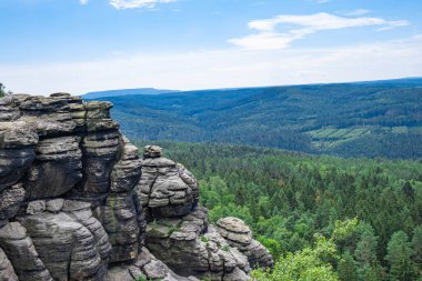 Mavi gökyüzü ve kayalık dağ zirvesi, bitki örtüsüyle kaplı dağlık arazi.