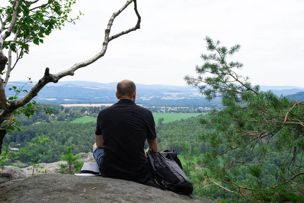 a seated man on the top of a mountain looks at the unfolding bird\'s-eye view