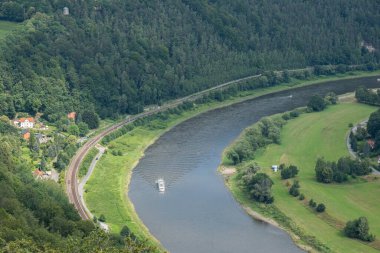 Elbe nehri akıyor ve bir buharlı gemi yol alıyor, evler sahil boyunca yer alıyor ve birçok ağaç yetişiyor.