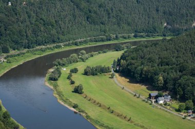 Elbe Nehri 'nin keskin bir virajı ve çeşitli ağaçlarla dolu bir orman, kıyı boyunca eski evler duruyor.