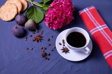 Sıcak kahve, rusk, olgun üç incir, dağınık kahve çekirdekleri, anason ve mavi arka planda bir dal ortanca tezgahı.