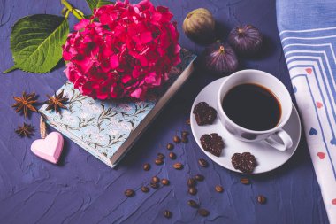 aromaton kahve, kitap ve pembe ortanca parçacıkları koyu çikolata ve üç incir mavi desenli arka planda yatıyor.