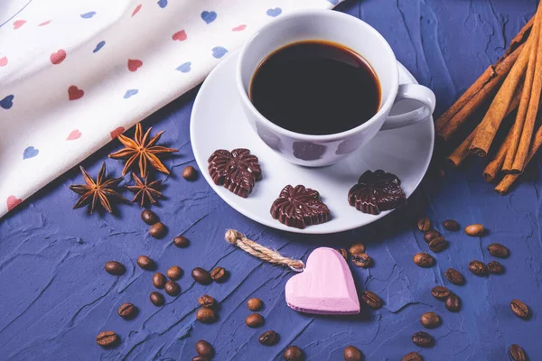 Bir fincan sıcak kahve, çikolata, tarçın ve desenli kahve çekirdekleri.
