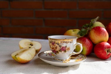 Masanın üzerinde bir fincan aromatik çay, olgun ve sulu elmalar var.