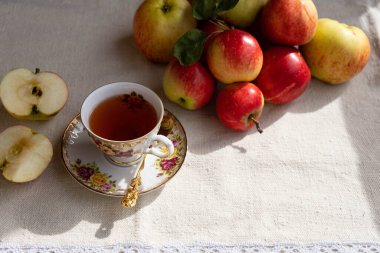 Çok güzel bir fincan çay, bir elmanın iki yarısı ve sağda bir kaç tam elma var.