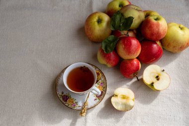 Çok güzel bir fincan çay ve bir elmanın iki yarısı var. Sağda da da birkaç koca elma var.