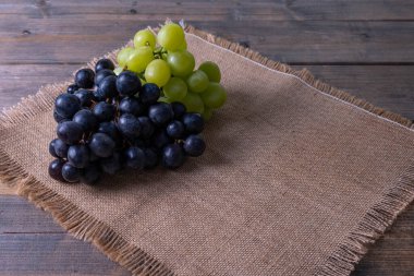 Olgun sulu üzüm hasadı kümeleri ahşap bir masa ve pürüzlü bir masa örtüsünün üzerinde yatıyor.