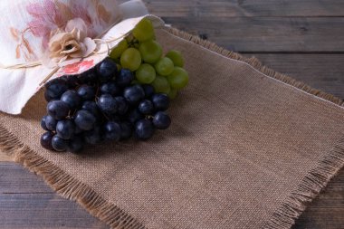 Olgun sulu üzüm hasadı kümeleri bir şapka ile kaplıdır ve ahşap bir masa ve pürüzlü bir masa örtüsü üzerine uzanır.