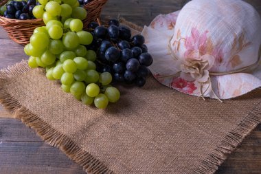 Olgun yeşil ve siyah üzüm demetleri tahta bir masa ve masa örtüsünün üzerinde yatıyor.