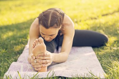 Parkta yoga yapan beyaz bir kadın. Oturup esnemek