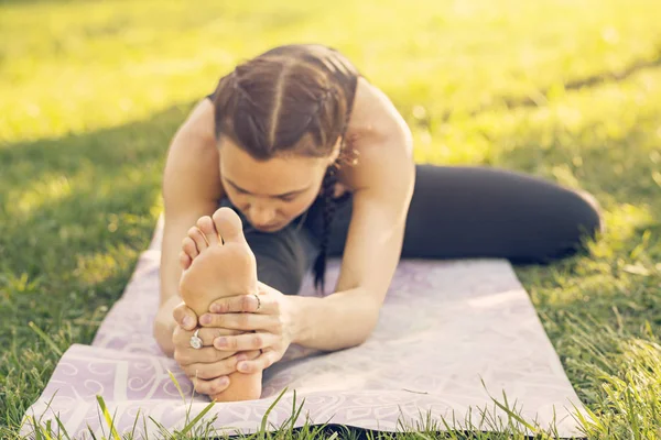 Junge kaukasische Frau beim Yoga im Park. Sitzen und Strecken lizenzfreie Stockbilder