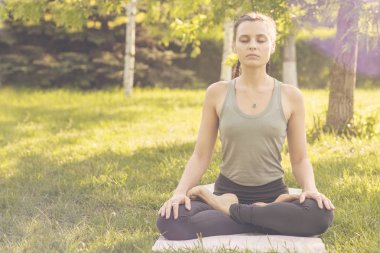 Parkta yoga yapan beyaz bir kadın. Lotus 'ta oturuyor.