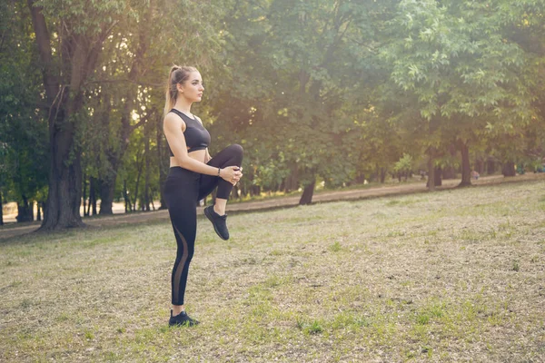 A young woman makes stretching legs in the Park. Does squat — Stock Photo, Image