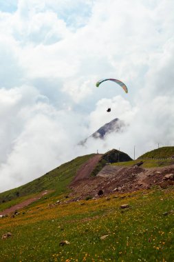 bulutlu bir dağ manzarasının arka planında uçan bir paraglider.