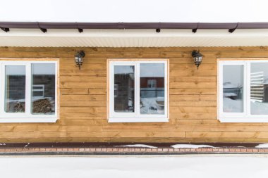 Ahşap bir ev büyük pencereler ve dış ışıkları ile korumasız cephe.