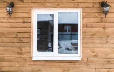 Ahşap bir ev geniş pencere ve dış ışıkları ile korumasız cephe.