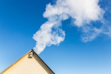 Mavi gökyüzüne karşı evin baca duman gelir. Boru çatıda. Baca. Kır evi.