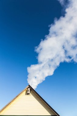 Mavi gökyüzüne karşı evin baca duman gelir. Boru çatıda. Baca. Kır evi.