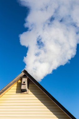 Mavi gökyüzüne karşı evin baca duman gelir. Boru çatıda. Baca. Kır evi.