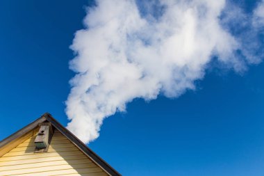 Mavi gökyüzüne karşı evin baca duman gelir. Boru çatıda. Baca. Kır evi.