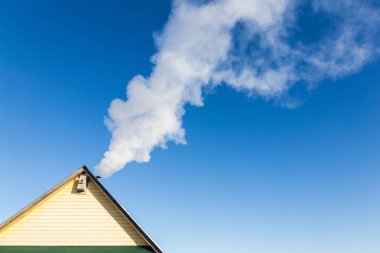 Mavi gökyüzüne karşı evin baca duman gelir. Boru çatıda. Baca. Kır evi.