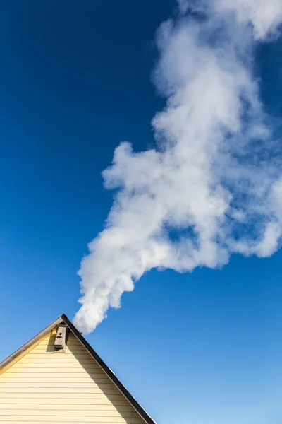 Smoke comes from the chimney of the house against the blue sky. The pipe on the roof. Chimney. Country house.