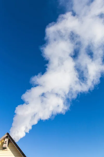 Smoke comes from the chimney of the house against the blue sky. The pipe on the roof. Chimney. Country house.