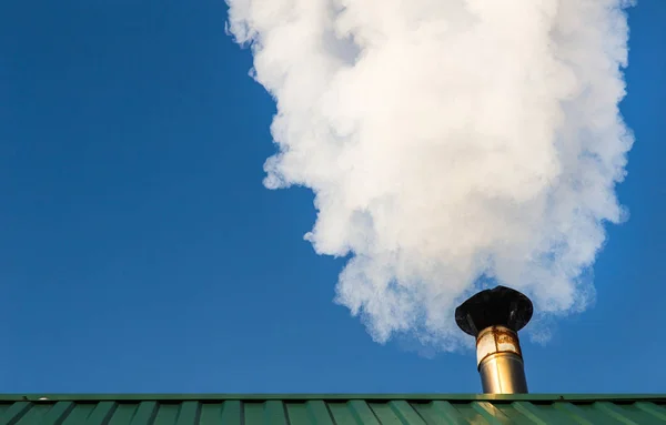 Smoke comes from the chimney of the house against the blue sky. The pipe on the roof. Chimney. Country house.