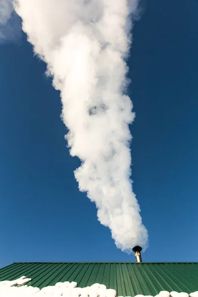 Smoke comes from the chimney of the house against the blue sky. The pipe on the roof. Chimney. Country house.