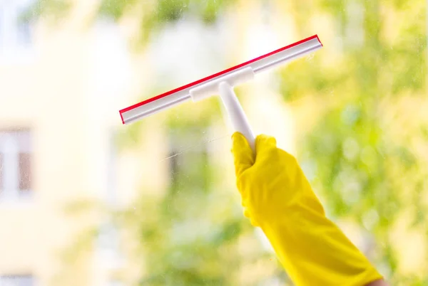 hand cleaning glass window pane with detergent and rubber aluminum wiper. A female hands in bright yellow gloves washes the windows