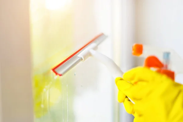 hand cleaning glass window pane with detergent and rubber aluminum wiper. A female hands in bright yellow gloves washes the windows