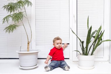 Küçük oğlu arasında çiçek kör bir arka plan üzerinde kırmızı bir tişört içinde bir pencere pervazına oturur