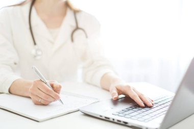 bir sabahlık bir stetoskop ile doktor bir masada oturur ve bir dizüstü bilgisayarda çalışır. Medecine, tanılama ve modern teknolojiler