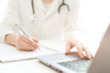 bir sabahlık bir stetoskop ile doktor bir masada oturur ve bir dizüstü bilgisayarda çalışır. Medecine, tanılama ve modern teknolojiler